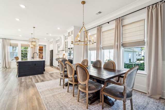 dining space featuring ornamental molding, sink, light hardwood / wood-style flooring, and a notable chandelier