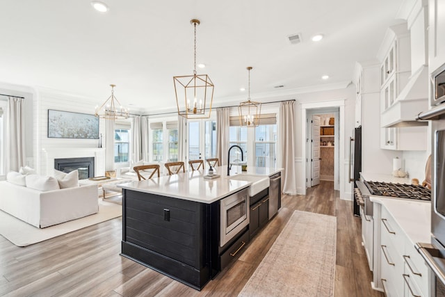 kitchen featuring white cabinets, decorative light fixtures, sink, and an island with sink