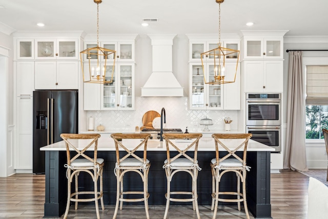 kitchen with custom exhaust hood, stainless steel appliances, a center island with sink, and pendant lighting