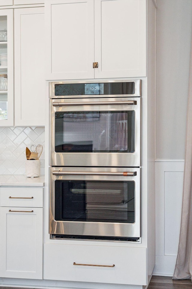 kitchen featuring double oven, white cabinetry, decorative backsplash, and wood-type flooring