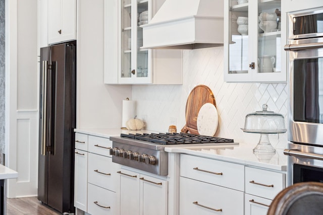 kitchen with backsplash, appliances with stainless steel finishes, white cabinetry, premium range hood, and dark hardwood / wood-style flooring