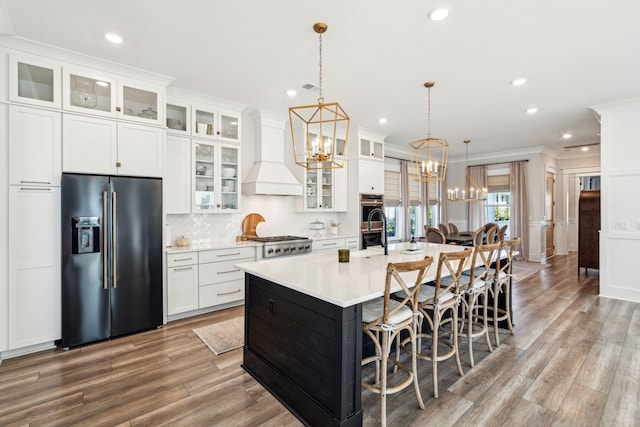 kitchen featuring custom exhaust hood, a center island with sink, appliances with stainless steel finishes, ornamental molding, and decorative light fixtures