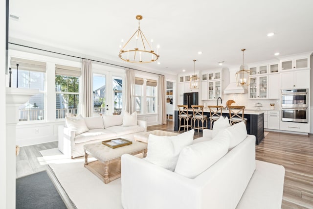 living room featuring french doors, light hardwood / wood-style flooring, ornamental molding, sink, and a chandelier