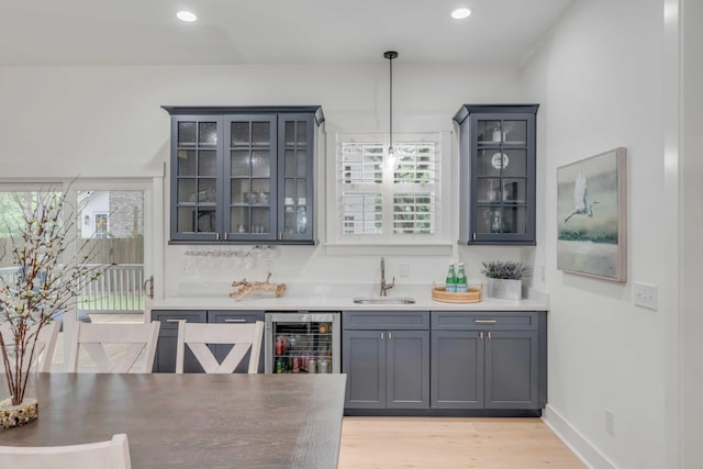 bar with gray cabinets, decorative light fixtures, sink, beverage cooler, and light hardwood / wood-style flooring