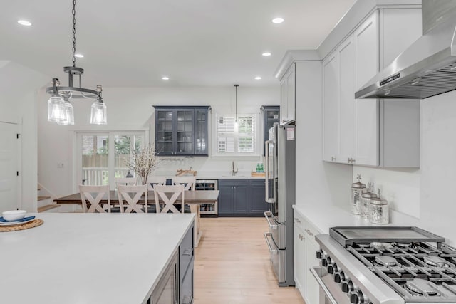 kitchen with light hardwood / wood-style flooring, gray cabinetry, hanging light fixtures, premium appliances, and wall chimney exhaust hood