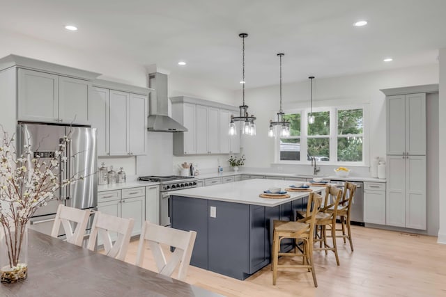 kitchen featuring light hardwood / wood-style floors, premium appliances, hanging light fixtures, a center island, and wall chimney range hood