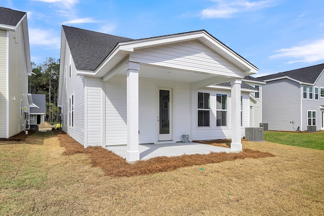 view of front facade featuring a patio area, a front lawn, roof with shingles, and central AC unit