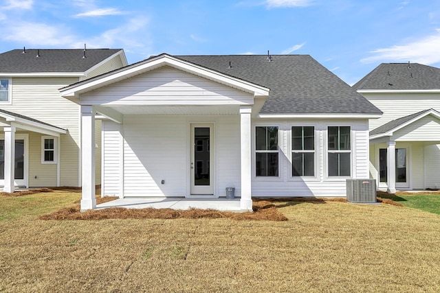 rear view of property featuring cooling unit, a patio area, a lawn, and a shingled roof