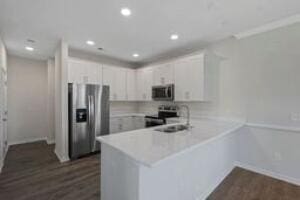 kitchen with stainless steel appliances, a peninsula, dark wood-style flooring, white cabinetry, and light countertops