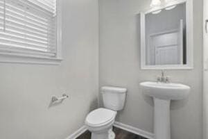 half bath with a sink, toilet, and baseboards