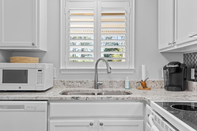 kitchen with light stone counters, white appliances, a sink, and white cabinetry