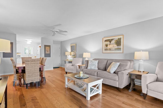 living area featuring light wood-style floors, ceiling fan, and baseboards