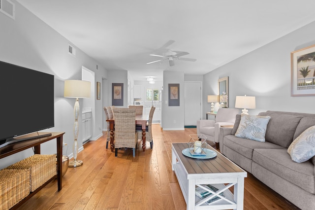 living area with ceiling fan, baseboards, visible vents, and light wood-style floors