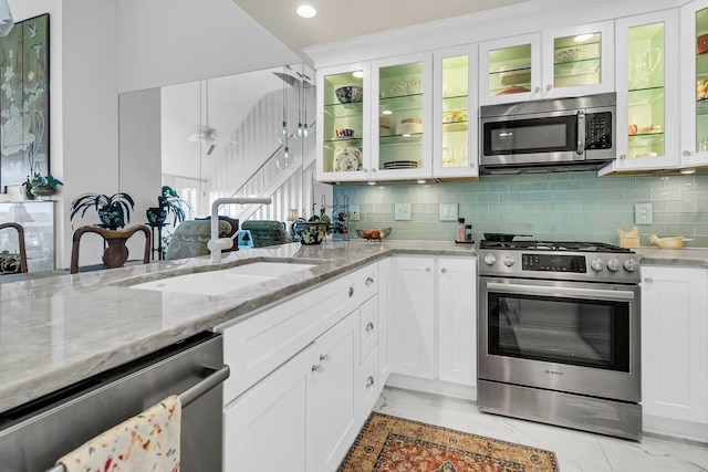 kitchen featuring backsplash, stainless steel appliances, white cabinetry, ceiling fan, and light stone counters