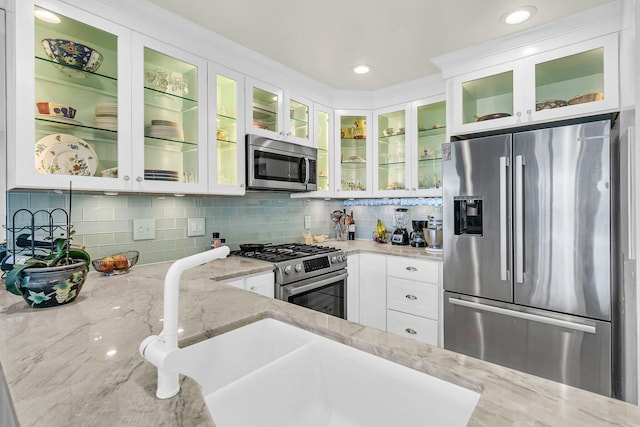 kitchen featuring light stone countertops, stainless steel appliances, white cabinetry, sink, and decorative backsplash