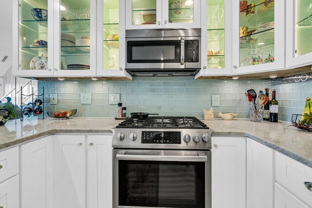 kitchen with stainless steel appliances, light stone countertops, decorative backsplash, and white cabinets