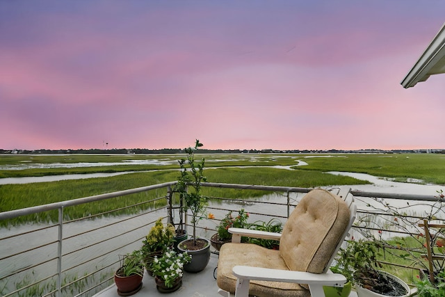 balcony at dusk featuring a water view