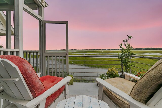 balcony at dusk featuring a water view