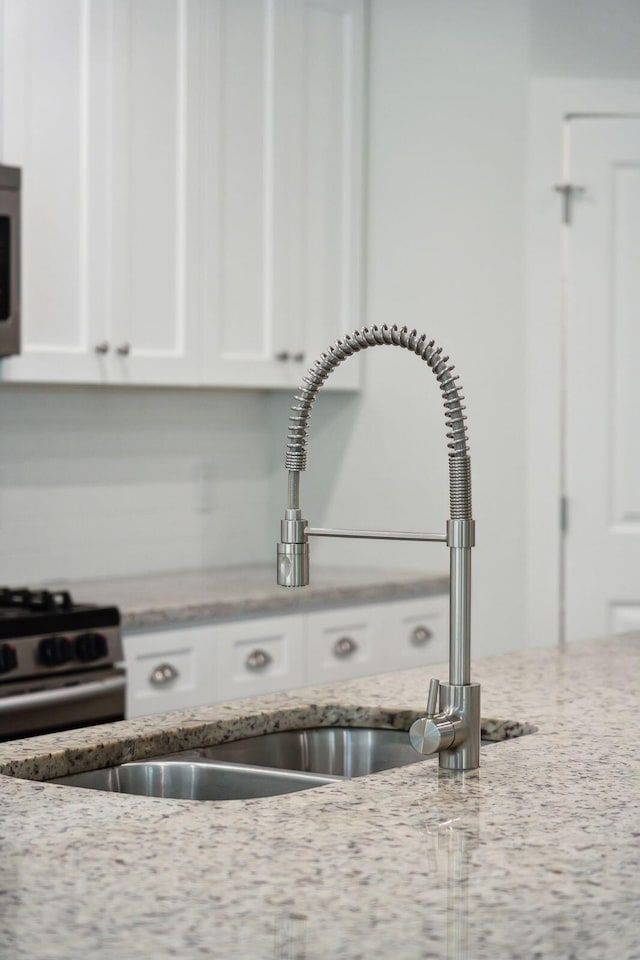 interior details featuring white cabinetry, light stone countertops, sink, and stainless steel gas range