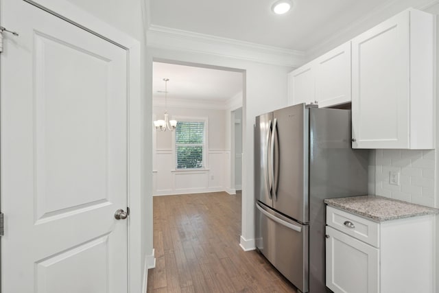 kitchen featuring hardwood / wood-style flooring, stainless steel fridge, light stone countertops, ornamental molding, and white cabinets