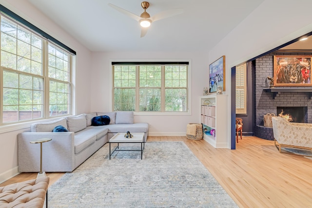 living room with a brick fireplace, ceiling fan, and wood-type flooring