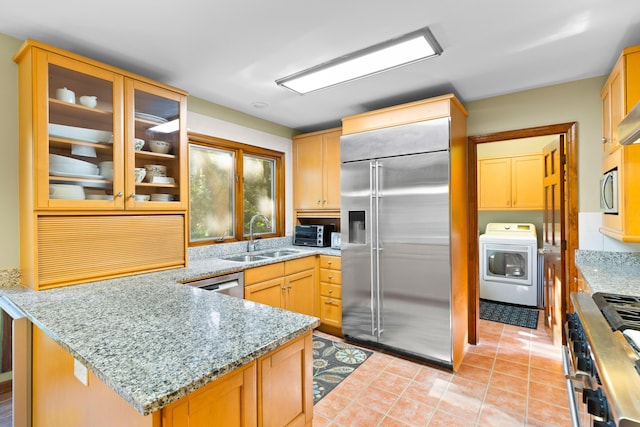 kitchen featuring high quality appliances, sink, light tile patterned flooring, light stone counters, and washer / clothes dryer