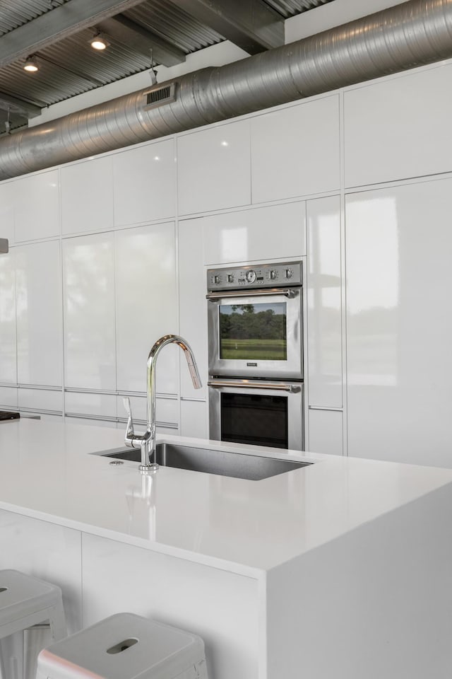 kitchen with white cabinets, sink, a breakfast bar, and stainless steel double oven