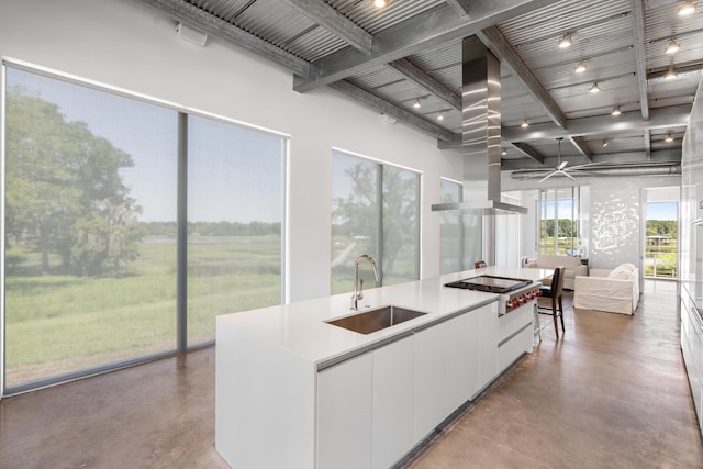 kitchen featuring stainless steel gas cooktop, sink, an island with sink, beam ceiling, and white cabinetry