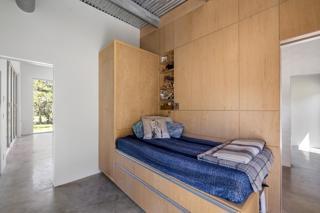 bedroom featuring concrete flooring, beamed ceiling, and a high ceiling