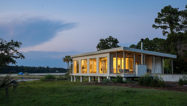 back house at dusk featuring a water view and a lawn