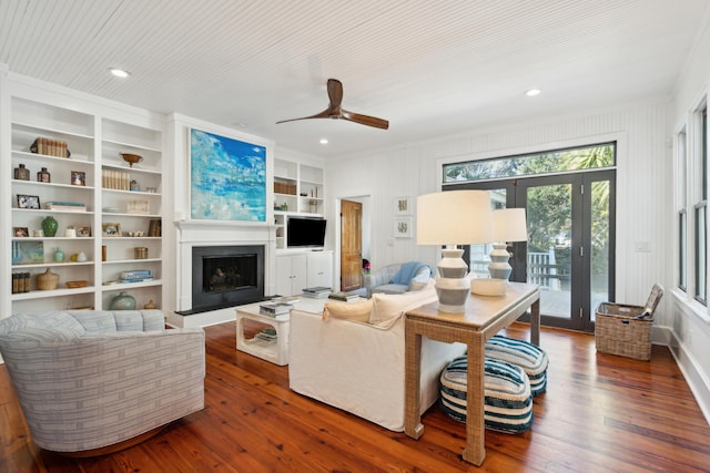 living room featuring built in features, ceiling fan, crown molding, and dark hardwood / wood-style floors