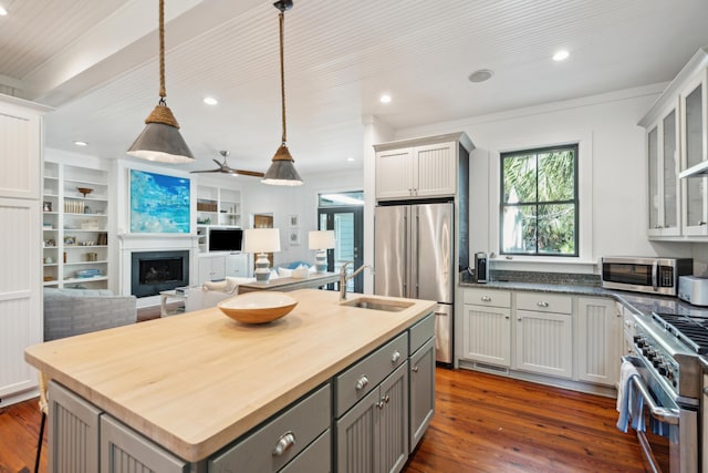 kitchen featuring premium appliances, decorative light fixtures, built in shelves, an island with sink, and gray cabinets