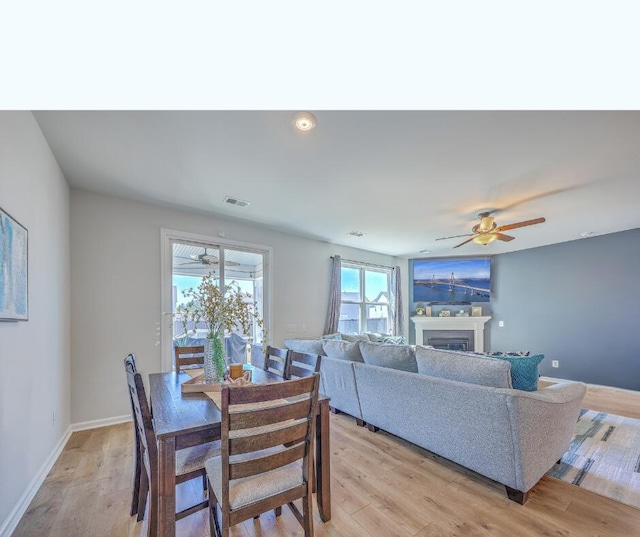 dining area featuring light wood-type flooring, a fireplace, visible vents, and baseboards