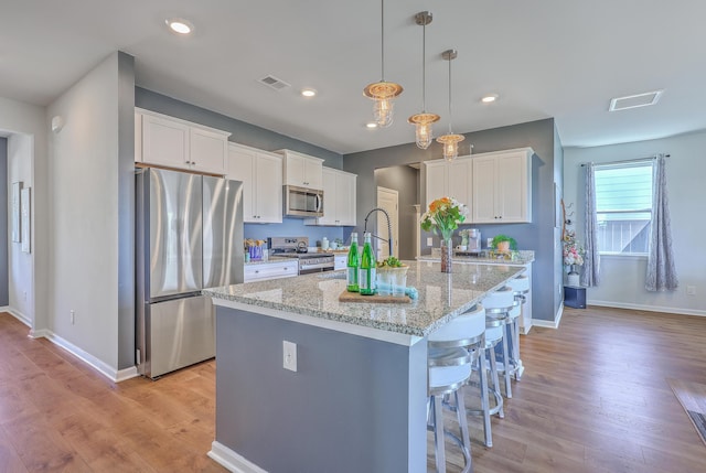 kitchen with light wood finished floors, visible vents, white cabinets, an island with sink, and appliances with stainless steel finishes