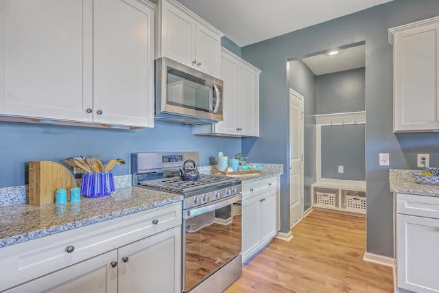 kitchen featuring light stone counters, light wood-style flooring, stainless steel appliances, baseboards, and white cabinets