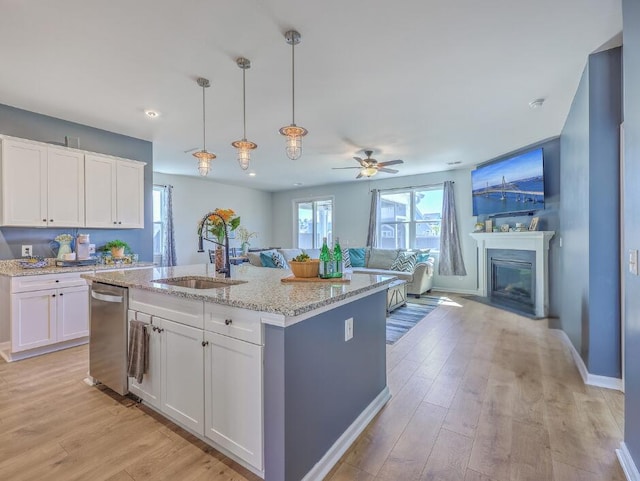 kitchen featuring a sink, light wood-type flooring, dishwasher, and a glass covered fireplace