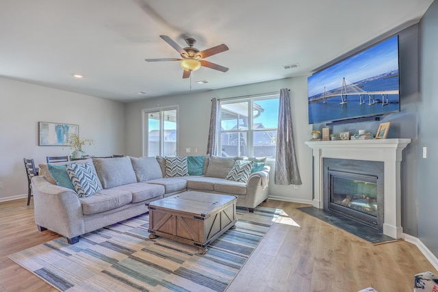 living room with baseboards, visible vents, wood finished floors, and a glass covered fireplace