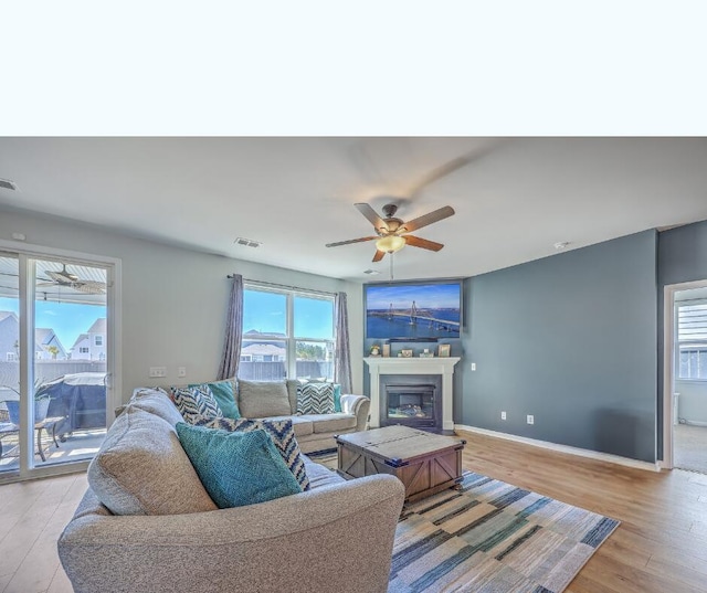 living room featuring a ceiling fan, visible vents, baseboards, light wood-type flooring, and a glass covered fireplace