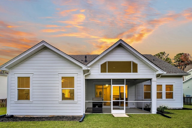 back house at dusk featuring a lawn, a patio area, and a sunroom