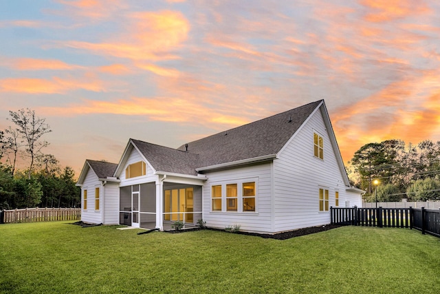 back house at dusk with a sunroom and a yard