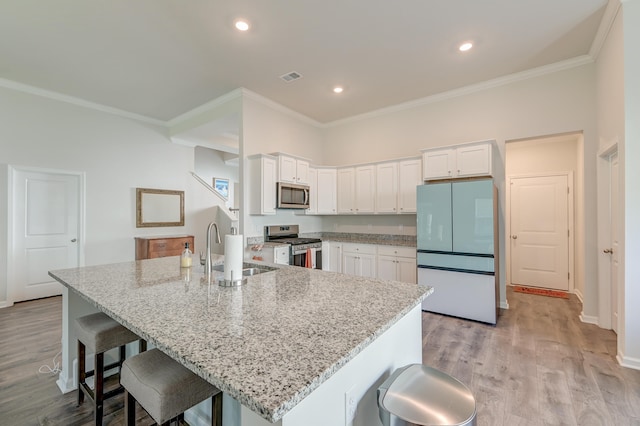 kitchen with white cabinets, stainless steel appliances, light stone countertops, and a kitchen island with sink