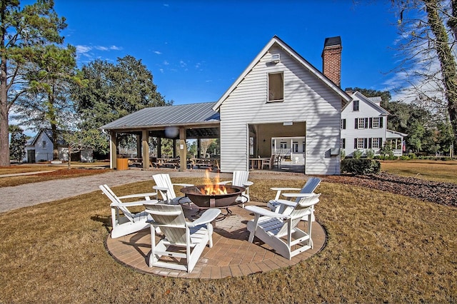 rear view of house with a fire pit, a patio, and a lawn