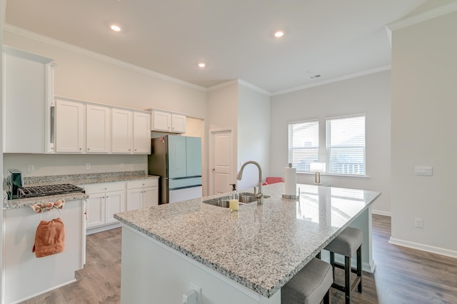 kitchen featuring light wood-type flooring, a kitchen island with sink, sink, white cabinets, and stainless steel refrigerator