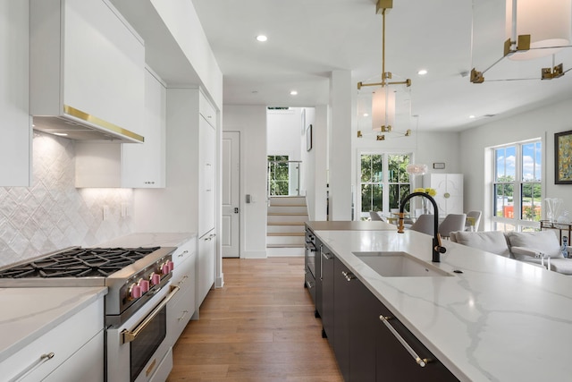 kitchen with light stone counters, sink, pendant lighting, high end stainless steel range, and white cabinetry