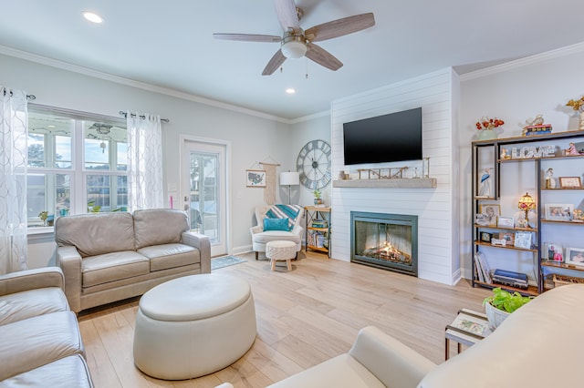 living room featuring ornamental molding, light hardwood / wood-style floors, a large fireplace, and ceiling fan