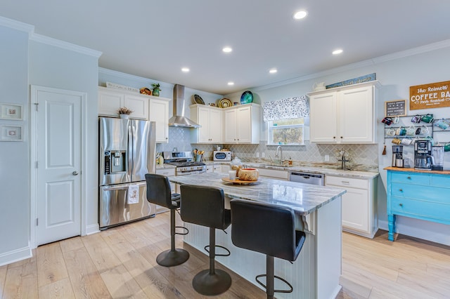 kitchen with wall chimney range hood, stainless steel appliances, light stone counters, white cabinets, and a kitchen island