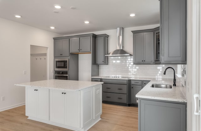 kitchen featuring sink, a kitchen island, stainless steel appliances, wall chimney exhaust hood, and light hardwood / wood-style flooring