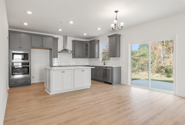 kitchen featuring a kitchen island, appliances with stainless steel finishes, light hardwood / wood-style flooring, gray cabinets, and wall chimney exhaust hood