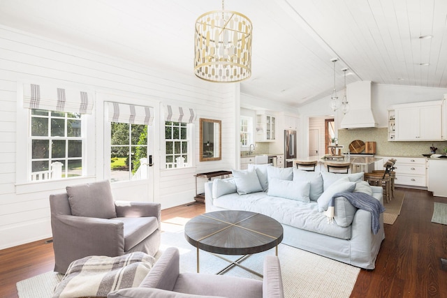 living room featuring dark hardwood / wood-style floors, wooden walls, lofted ceiling, sink, and an inviting chandelier