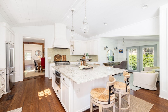 kitchen with vaulted ceiling, appliances with stainless steel finishes, white cabinetry, custom exhaust hood, and light stone counters